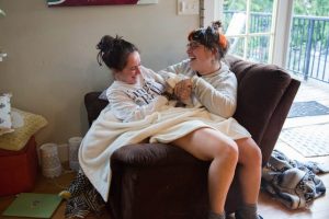 Jordan Coady and Chloe Fleuret laugh while sitting together on a recliner at home. The time at home has strengthened their relationship, both as roommates and friends.